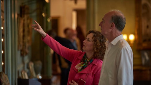 Two visitors stood side by side looking at a painting, one of them is pointing towards it.